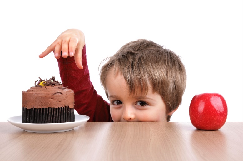 Boy choosing between apple and a cupcake, trying to make the healthy choice