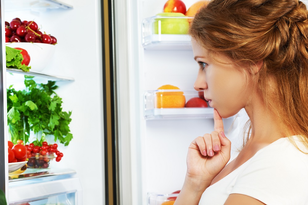 Happy woman standing at the open refrigerator with fruits, vegetables and healthy food. Learn which foods you should choose to lose weight.
