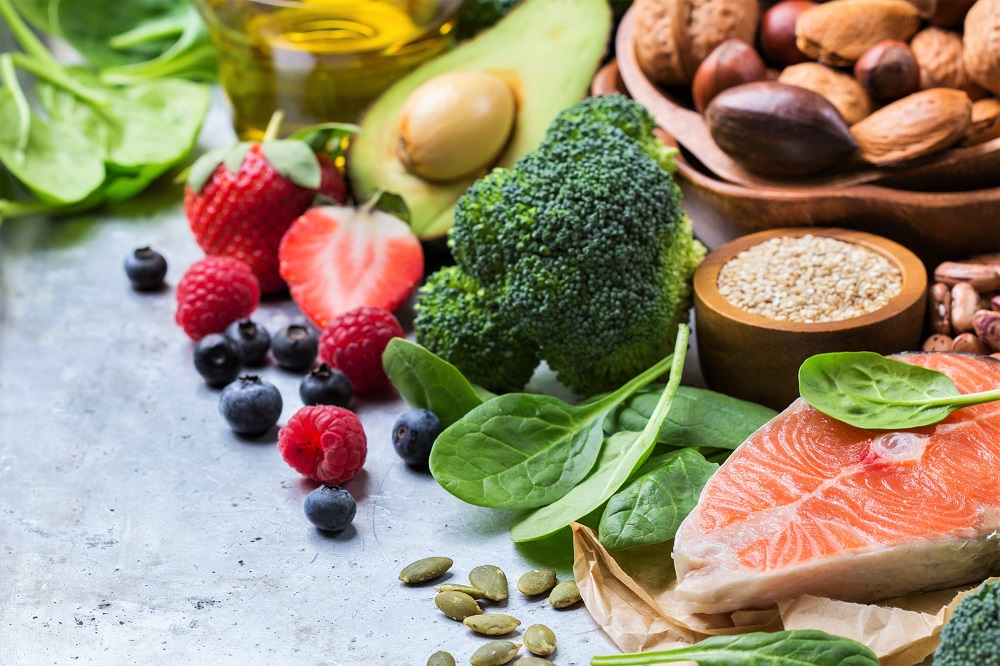 Broccoli berries avocado fish, spinach, and nuts on a grey surface- Preparing for weight loss by healthy grocery shopping and meal prepping for weight loss