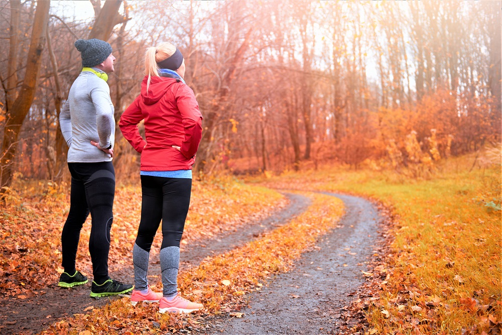 Man and woman in exercise gear on an autumn path, about to begin their weight loss journey