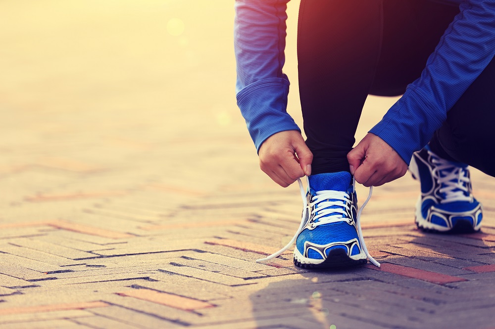 Person tying a blue shoe on a brick path- Preparing to exercise and lose weight