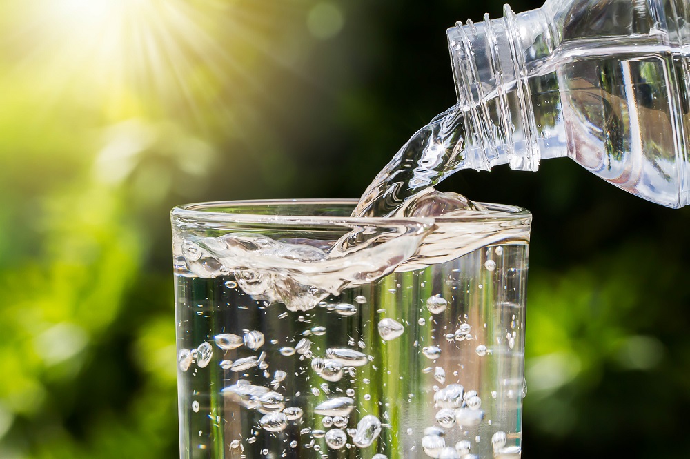 Clear water pouring into a glass on a sunny day with green trees in the background- Simple things you can do to lose weight without having to be hungry