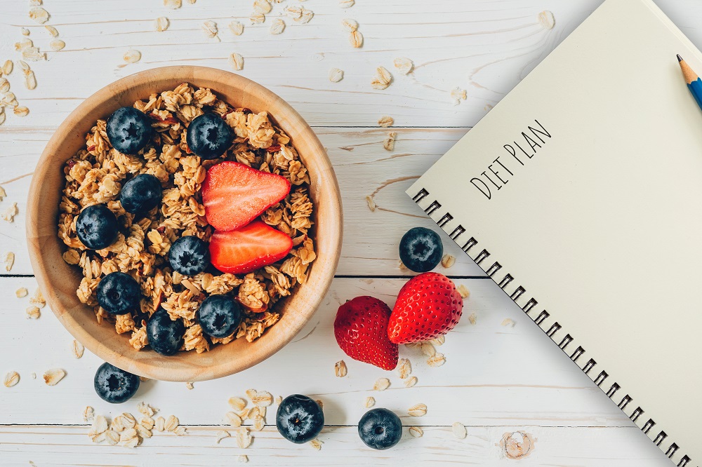 A notebook that says "Diet Plan", sitting next to a healthy bowl of oats and berries