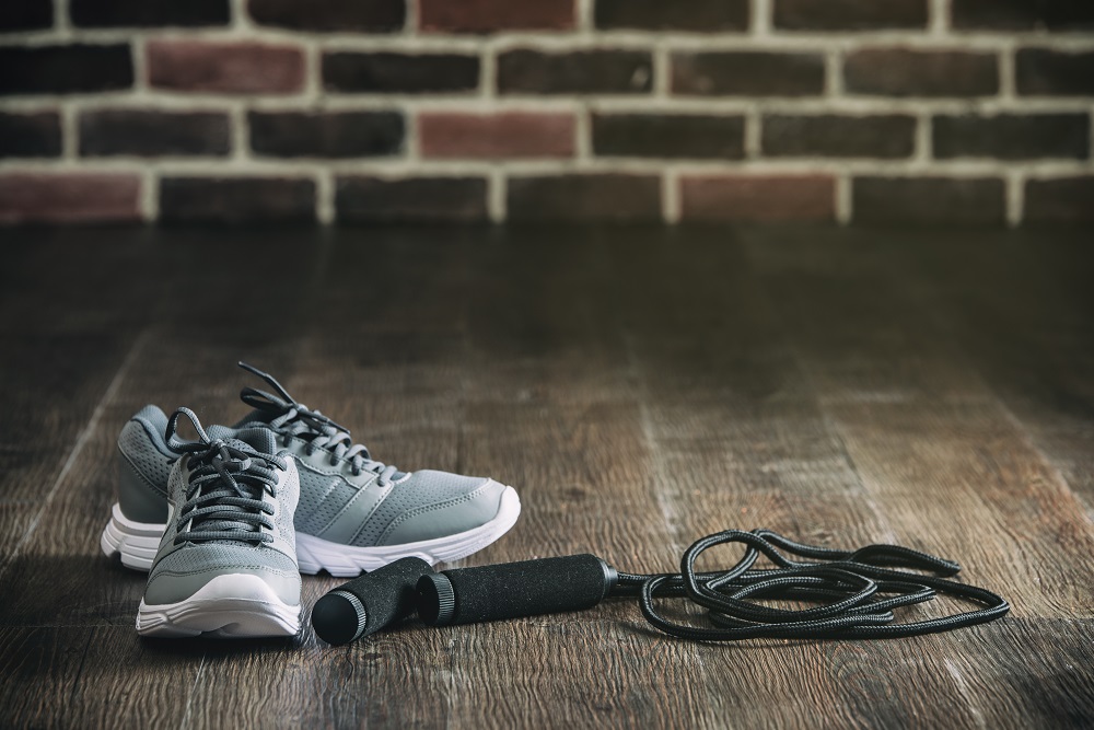 Grey shoes sitting next to a black jump rope, on a wooden floor that has sunlight shining on its surface