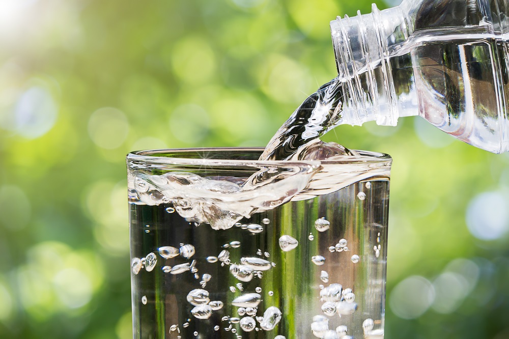 Water pouring into a glass with a sunny day in the background